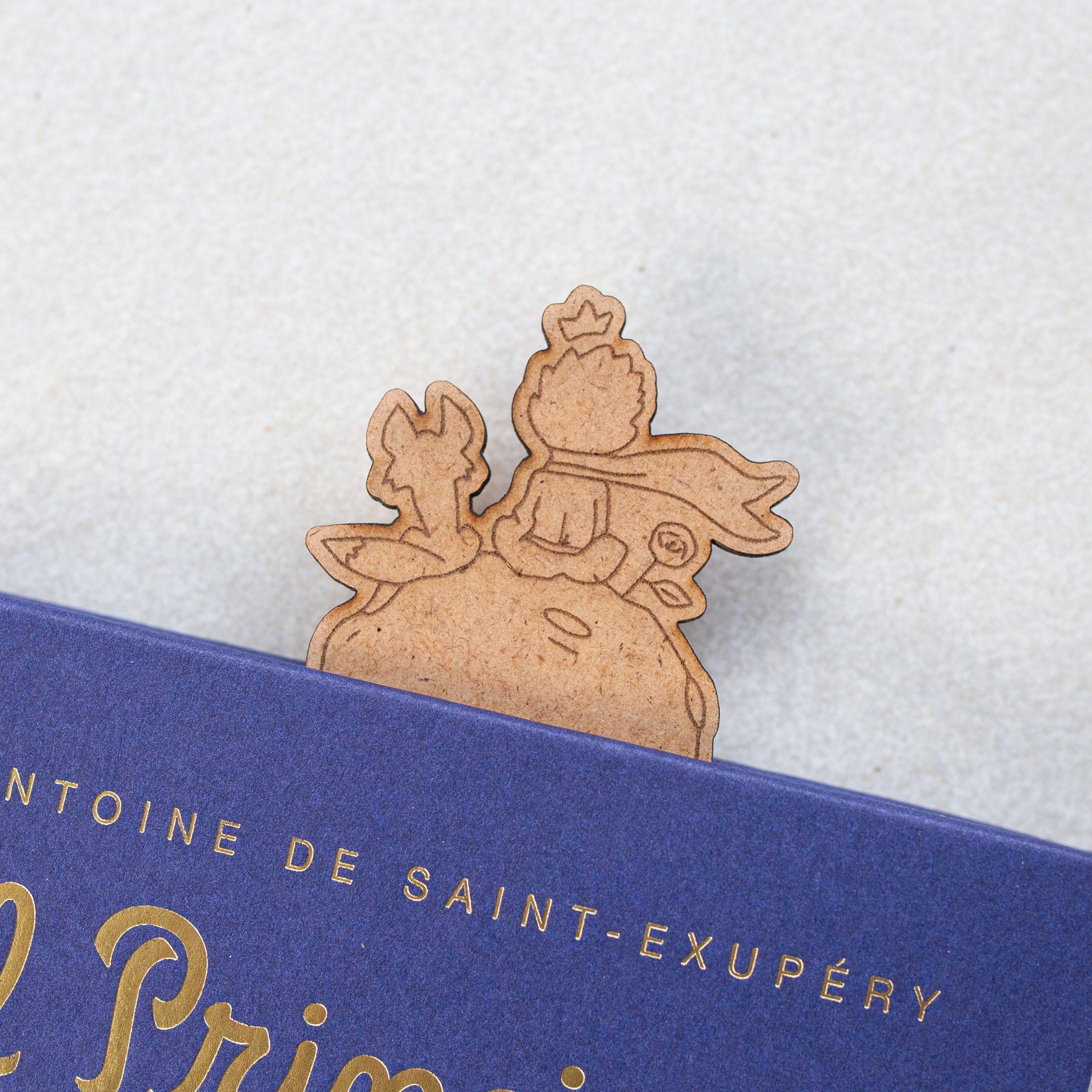 Marcapáginas de El Principito de madera para regalar Detalle de parte superior de marcapáginas de El Principito con el propio protagonista, el zorro y la rosa grabados. El marcapáginas se encuentra dentro de el libro de El Principito