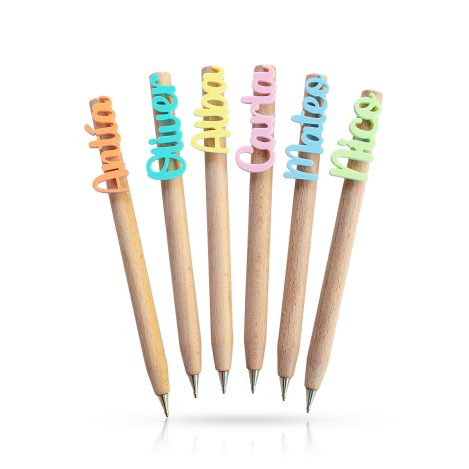 Seis bolígrafos de madera con nombres personalizados en metacrilato de colores naranja, verde aguamarina, amarillo, rosa, azul y verde pistacho. Los bolígrafos están situados sobre fondo blanco.
